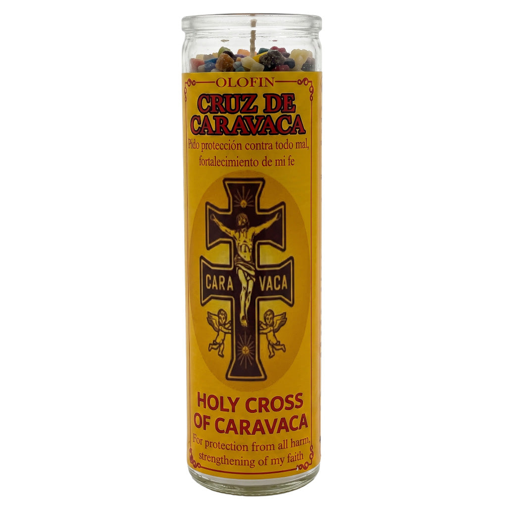 A tall glass jar candle with a yellow label reading 'Cruz de Caravaca' and 'Holy Cross of Caravaca,' featuring a black crucifix graphic and multicolored wax pieces visible at the top.