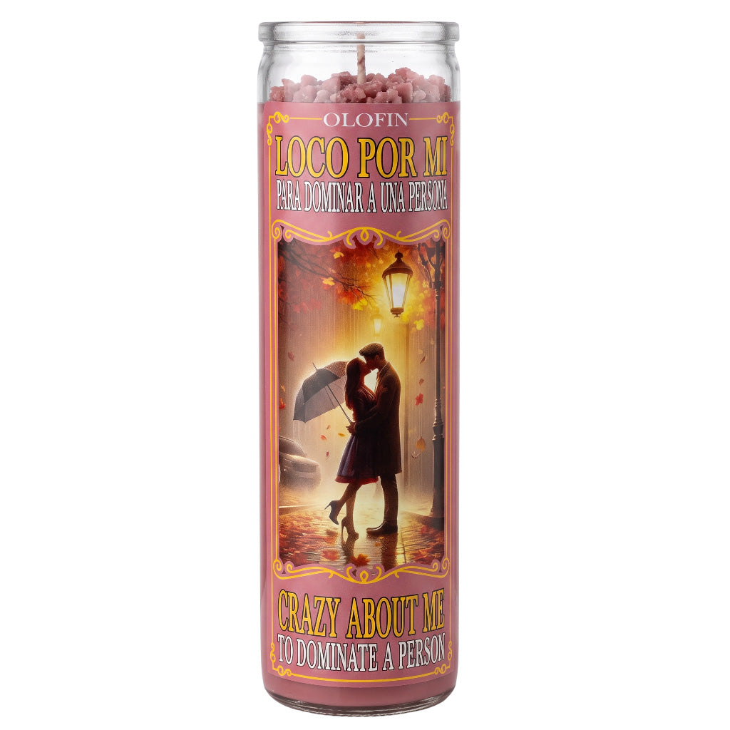 A tall glass jar candle with a pink and gold label reading 'LOCO POR MI' and 'CRAZY ABOUT ME TO DOMINATE A PERSON,' featuring an illustration of a couple under an umbrella in the rain.