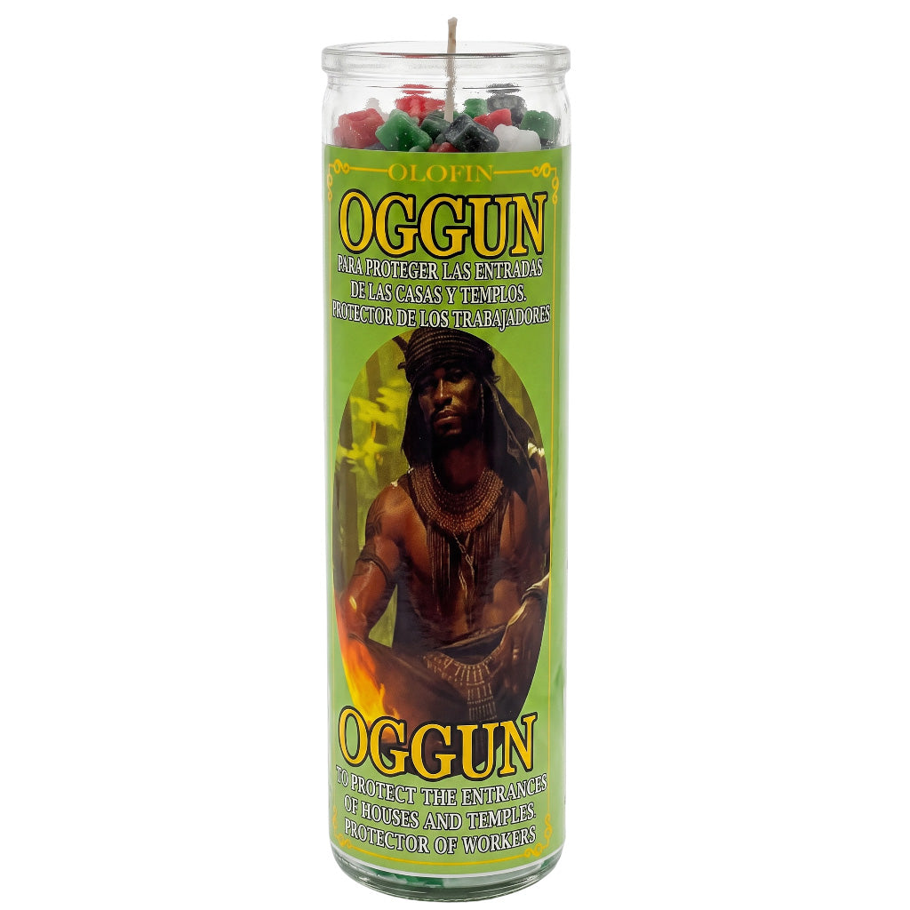 A tall glass jar candle labeled 'Oggun' with a green label featuring an illustration of a man and text in Spanish and English, shown on a plain white background.